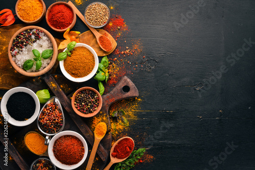Spices and herbs on a wooden board. Pepper, salt, paprika, basil, turmeric. On a black wooden chalkboard. Top view. Free copy space.