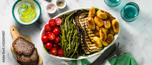 banner of a side dish of vegetables on the holiday table. healthy food for the whole family or dinner at a restaurant on a white marble table. baked potatoes, grilled eggplants, cherry tomato salad 