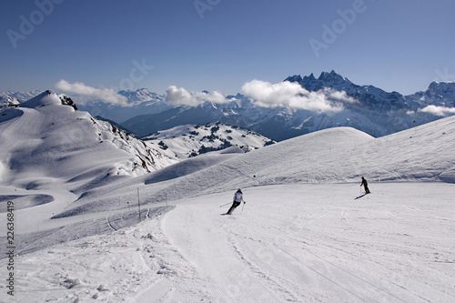 Skiers in French Alps carve turns as they make their way down a piste in Avoriaz, Portes du Soleil ski area. Swiss Alps can be seen in background