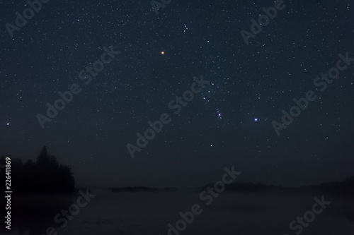 Orion constellation above misty lake.