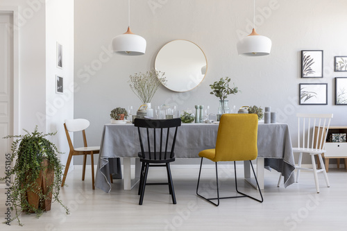 Black and yellow chair at table in white dining room interior with plants, lamps and mirror. Real photo