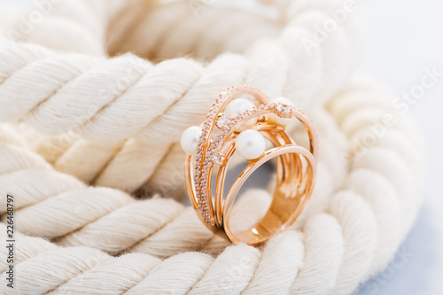 Stylish gold ring with pearls and diamonds on rope background