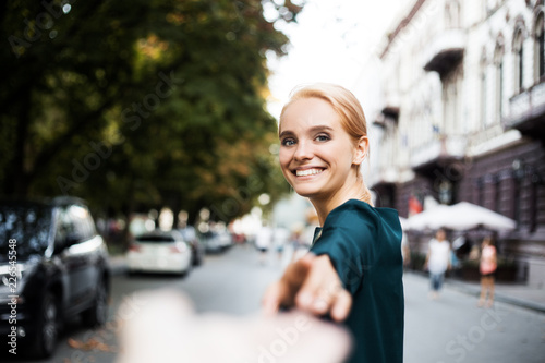 Follow Me. Young beautiful business woman in casual dress drags her boyfriend, spring street outdoors office after work going to restaurant and smiling because of free evening and weekend soon