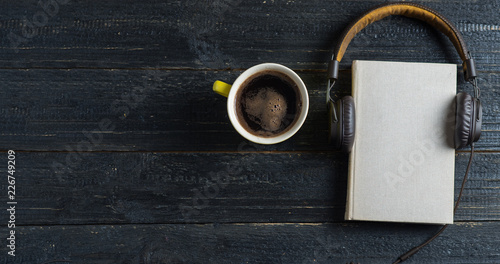 Audio book with headphones and coffee mug on dark wooden background. The concept of the electronic library