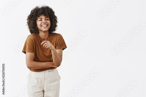 Studio shot of cute african american woman with afro hairstyle in trendy summer outfit having fun laughing out loud from joy and funny joke gesturing with palm chuckling and smiling carefree at camera