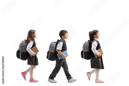 Three schoolchildren with backpacks and books walking