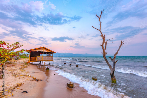 Burundi Bujumbura lake Tanganyika, windy cloudy sky and sand beach at sea lake in East Africa, Burundi sunset with house from wood and dead tree in the sea