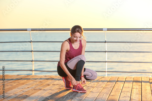 Young woman tying shoelaces on pier. Morning workout