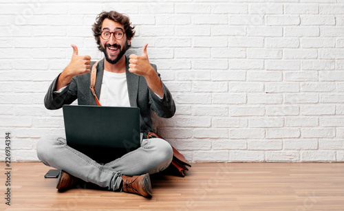 young man sitting on the floor with a satisfied, proud and happy look with thumbs up, signaling OK with both hands, sending a positive, "alright' message.