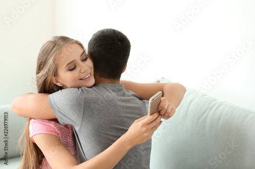 Young woman texting lover while hugging her boyfriend at home