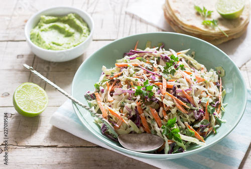 Coleslaw made from cabbage, carrots and various herbs, served with tortillas and guacamala on a wooden background.