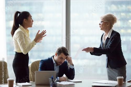 Mad middle aged businesswoman have dispute with young Asian employee blaming for mistake in documents, female partners conflict arguing at business meeting, accusing in contract failure