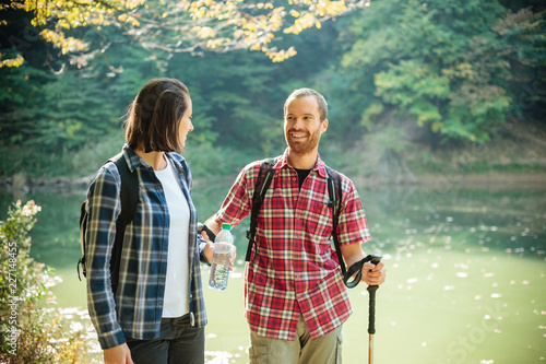 Smiling happy young couple in checkered shirts hiking along the lake shore, facing each other. Walking through forest on a beautiful autumn day. Healthy and active outdoor lifestyle
