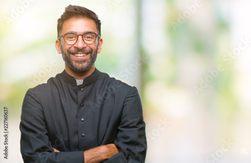 Adult hispanic catholic priest man over isolated background happy face smiling with crossed arms looking at the camera. Positive person.