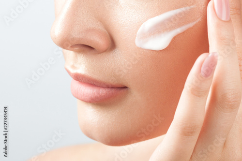 Young beautiful woman applies cream on clean perfect skin