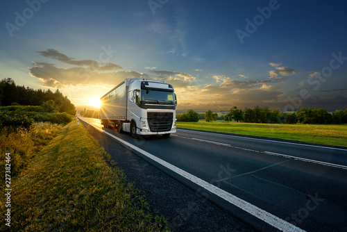 White truck driving on the asphalt road in rural landscape in the rays of the sunset