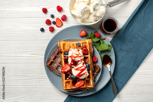 Delicious waffles with berries and ice cream on wooden table