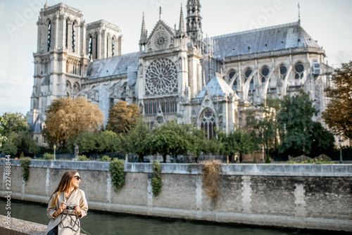 Young woman tourist sitting near the famous Notre Dame cathedral during the morning light traveling in Paris, France. Wide view with copy space