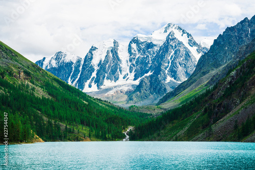 Wonderful giant snowy mountains. Creek flows from glacier into mountain lake. Shine water in highlands. White clear snow on ridge. Amazing atmospheric landscape of majestic Altai nature.
