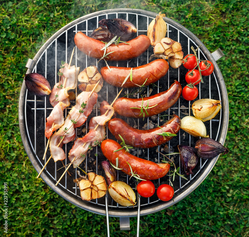 Grilled food. Grilled pork sausage, bacon and vegetables on the grill plate, top view, outdoor. Barbecue, bbq