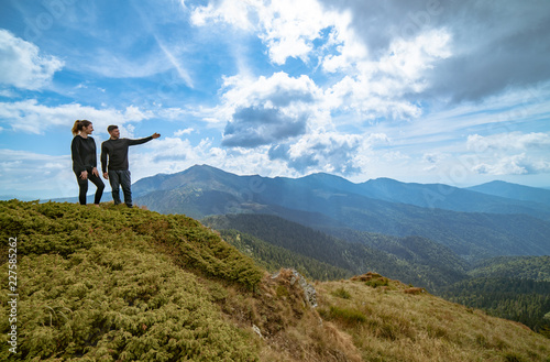 The couple gesturing on the mountain with a picturesque cloudscape