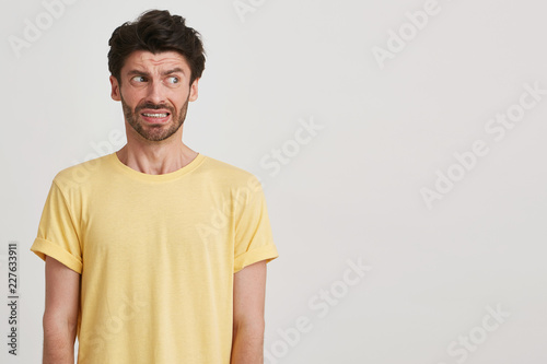 Clouse up of afraid fearful young man with dark brown hair and beard wears yellow casual tshirt, look right, standing left side isolated over white background