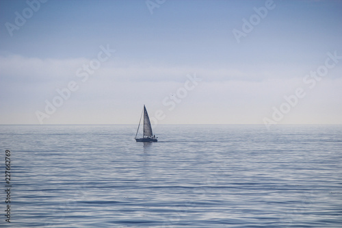 Sailboat on a distant hazy calm sea