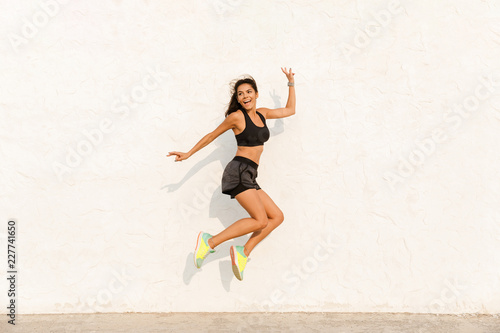 Full length image of european woman 20s in sportswear working out and running, along wall