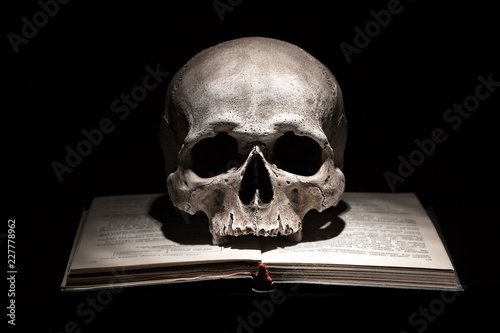 Human skull on old open book on black background. Dramatic concept.