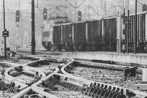 Railway tracks crossing with a blurred cargo train in the background (black and white image)