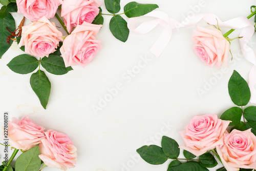 Rose fresh flowers frame with ribbon on table from above with copy space, flat lay scene