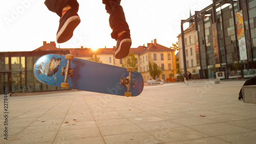 LOW ANGLE: Blue skateboard flipping underneath the young skateboarder's feet.