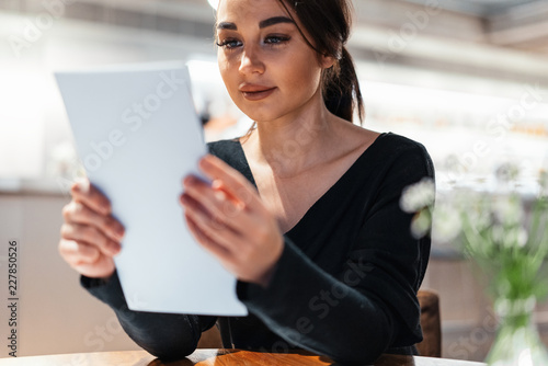 Young beautiful woman looking at menu deciding what to order in modern cafe.