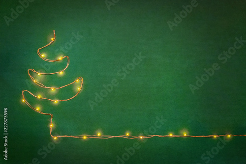 Christmas lights garland arranged like christmas tree over green background. Flat lay, copy space.