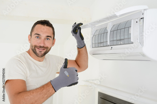 handsome young man electrician cleaning air filter on an indoor unit of air conditioning in a client house