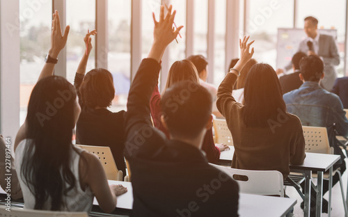 Raised up hands and arms of large group in seminar class room to agree with speaker at conference seminar meeting room