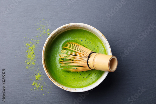 Matcha green tea cooking process in a bowl with bamboo whisk. Black slate background. Top view.