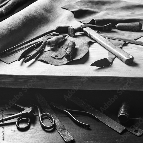 Old tools at table. Pieces of leather at cobbler workplace. Shoemaker's work desk. Leather craft tools on wooden background. Shoemaker tools. Shoemaker's shop. Black and white. Cobbler workmanship.