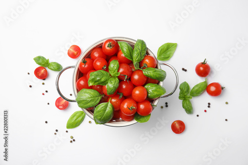 Colander with fresh green basil leaves and cherry tomatoes on white background, top view