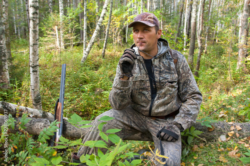 hunter sitting on a fallen tree and beckons grouse