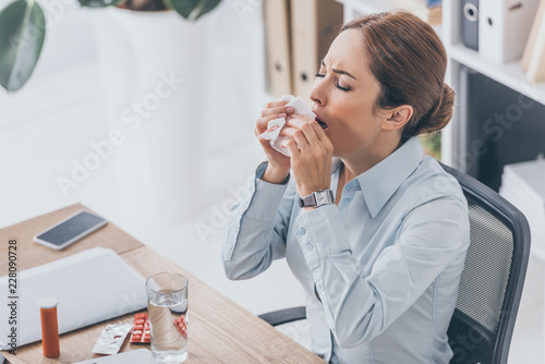 high angle view of diseased adult businesswoman sneezing at workplace