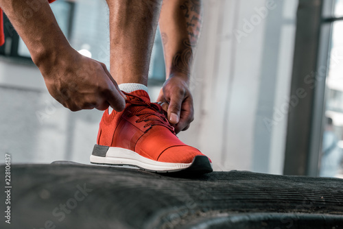 cropped image of sportsman tying laces of red sneakers at gym