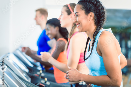 Side view of a fit happy woman and her training group on treadmill in the gym