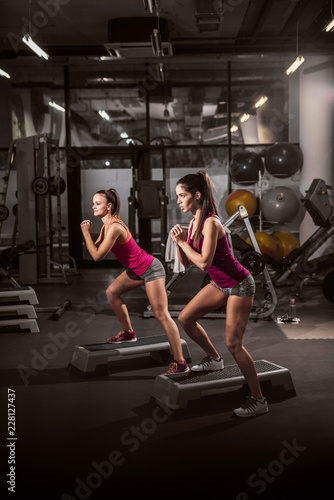 Two attractive women exercising on stepper in gym. Healthy lifestyle concept.