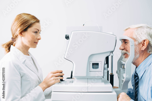 Doctor Optometrist examining old man's eyes with special eye equipment