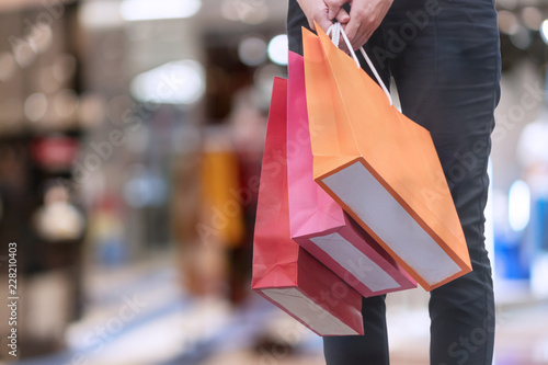 Hand of woman carrying shopping bags on shopping malls background. happiness, consumerism, sale and people concept.