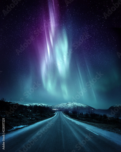 A quite road in Norway with a spectacular Northern Light Aurora display lighting up the night sky above the mountains. A popular destination within the arctic circle for hunting the Northern Lights.