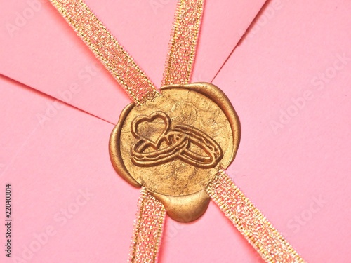 Złota pieczęć lakowa z obrączkami na różowej kopercie w zbliżeniu