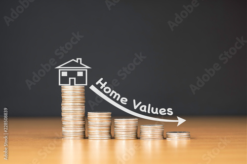 STACKED US QUARTER COINS ON WOODEN TABLE WITH WHITE ILLUSTRATION SHOWS DECREASING OF HOME VALUES / FINANCIAL CONCEPT