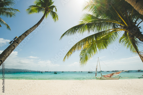 Perfect white sand beach in Boracay, Philippines. Coconut Palm trees against blue sky, boat in ocean. Sunny weather. Travel Background. Nature landscape. Holiday and recreation on exotic island resort